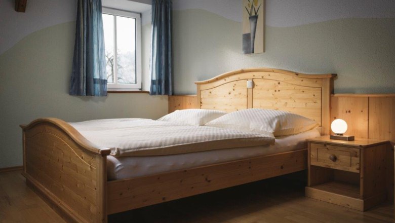 A bedroom with a wooden bed, bedside table and lamp, blue curtains and a picture on the wall.