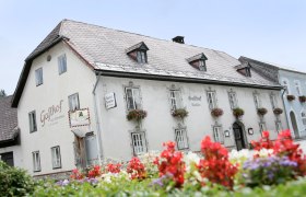 Ein traditionelles Gasthaus mit Blumen an den Fenstern und einem Schild mit der Aufschrift 'Gasthof Rauscher'.