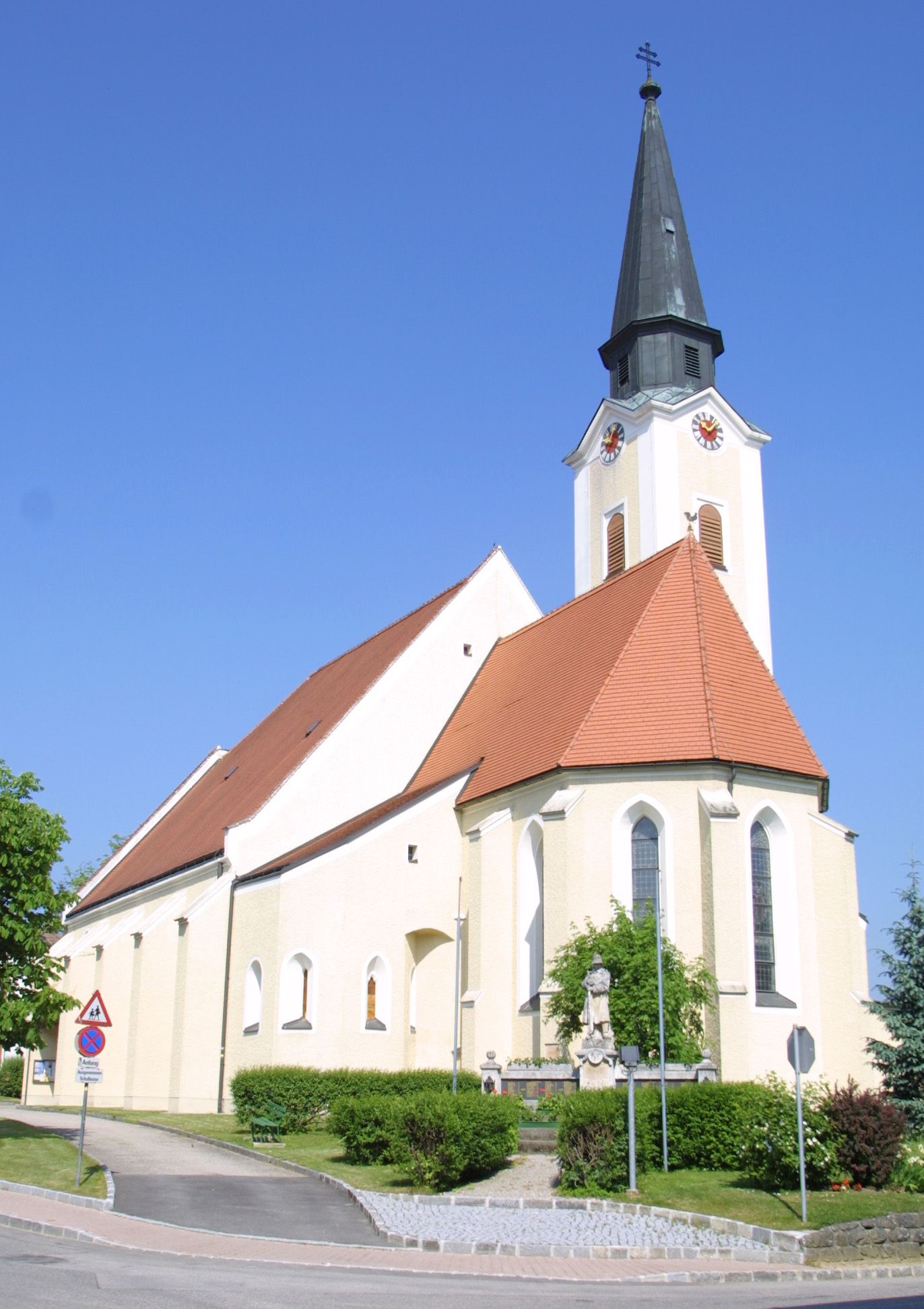 Kirche in Hürm mit spitzem Turm und rotem Dach vor blauem Himmel.