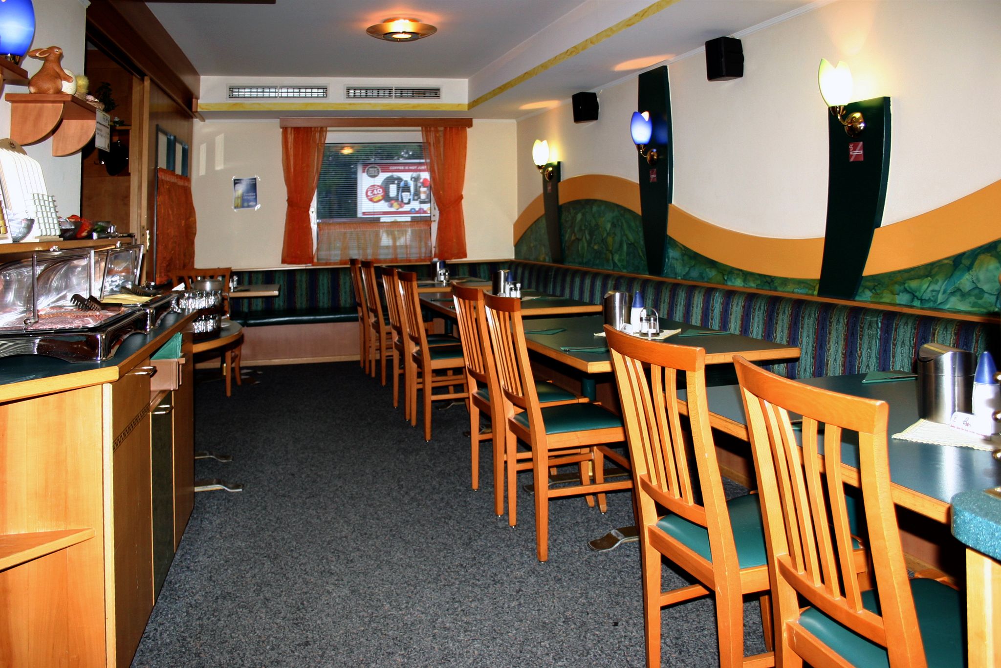 Innenansicht eines leeren Restaurants mit Holzmöbeln und grünen Polstern.