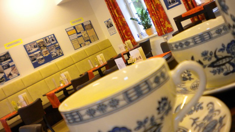 Innenansicht eines Cafés mit Teetassen im Vordergrund und dekorierten Wänden im Hintergrund.