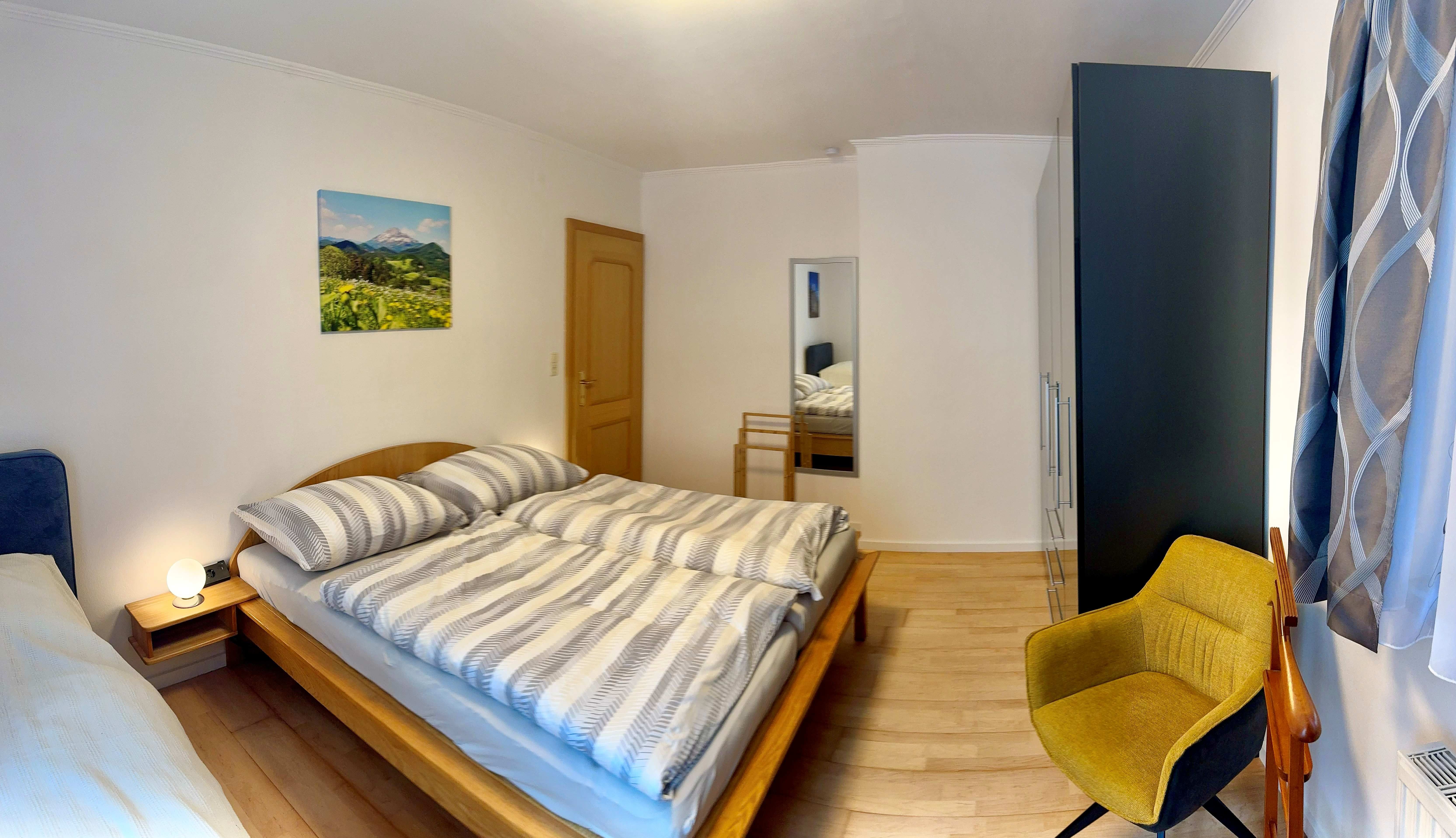 Ein Schlafzimmer mit einem Doppelbett, einem gelben Stuhl, einem Schrank.