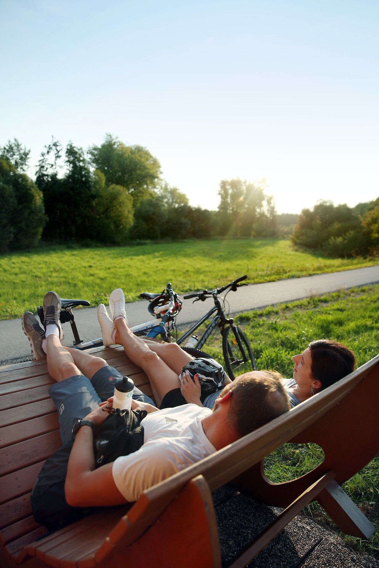 In der warmen Sommerluft entspannen zwei Radfahrer auf einer Bank und genießen die malerische Aussicht auf die sanften Hügel des Melker Alpenvorlands. Die Fahrräder stehen bereit für weitere Abenteuer in dieser idyllischen Landschaft, die zum Erkunden einlädt.