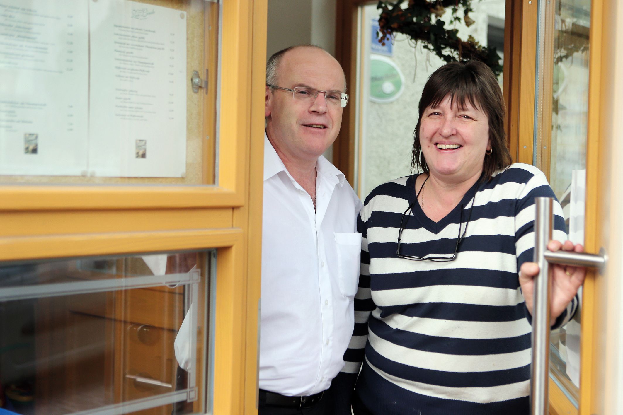 Ein Mann und eine Frau stehen lächelnd in einer Türöffnung eines Gebäudes.