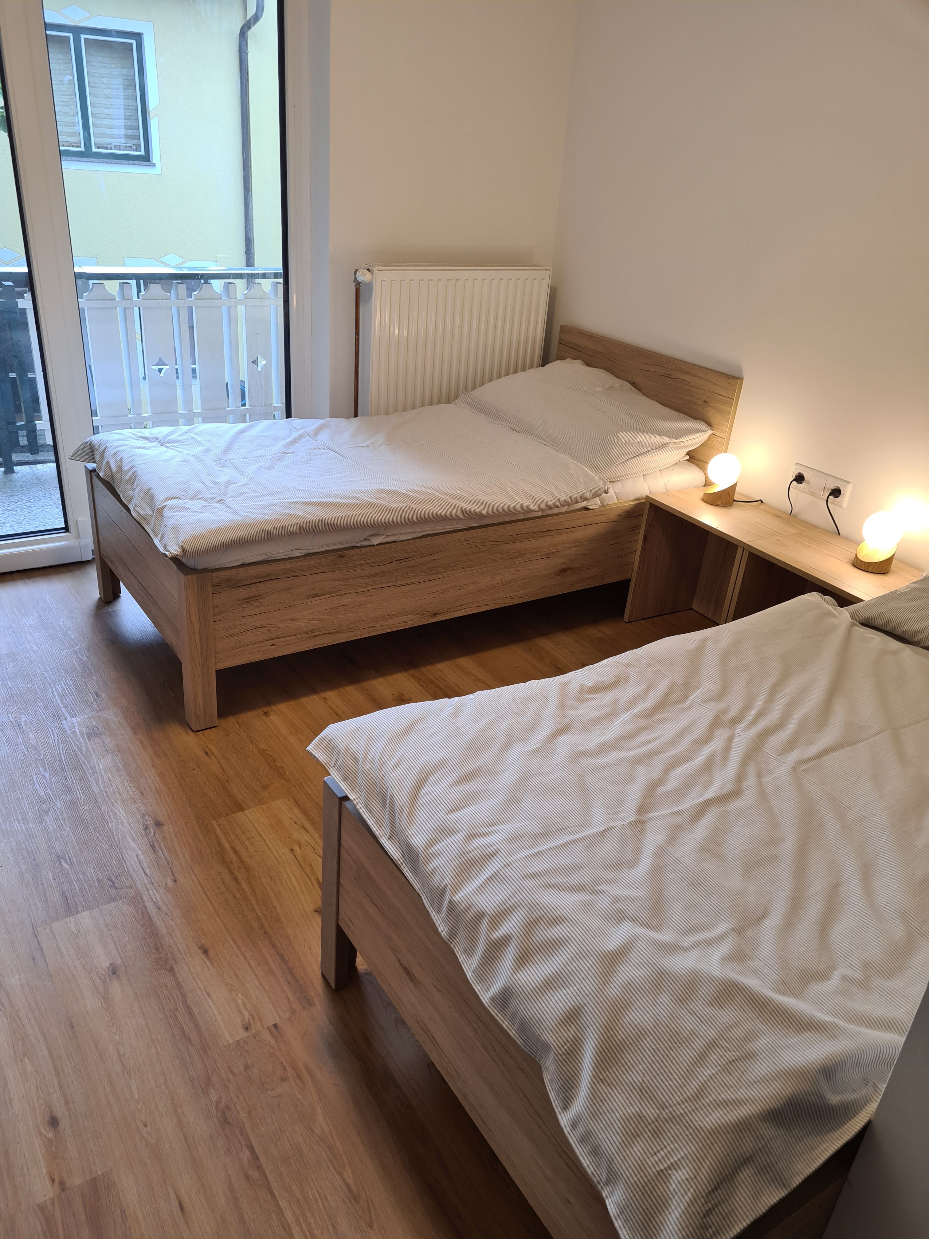 Zwei Einzelbetten in einem hellen Zimmer mit Holzboden und Balkonzugang.