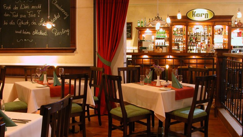Gem&uuml;tliches Restaurant mit Holzm&ouml;beln, gedeckten Tischen und einer Bar im Hintergrund.