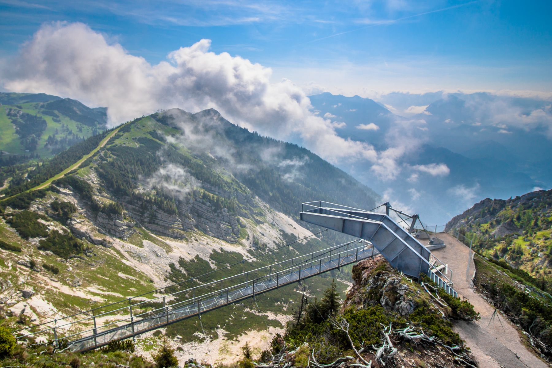 Aussichtsplattform auf einem Berg mit Wolken und grüner Landschaft.