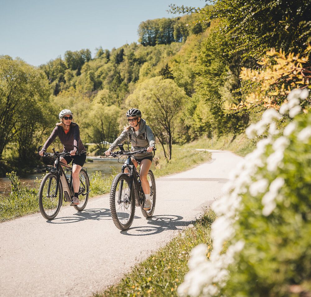 Zwei Radfahrerinnen fahren entlang des Traisental-Radwegs, der durch bewaldetes Gebiet führt.