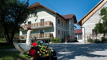 Ein Bauernhof mit einem grünen Haus, Blumen und einer Gänsestatue im Vordergrund.