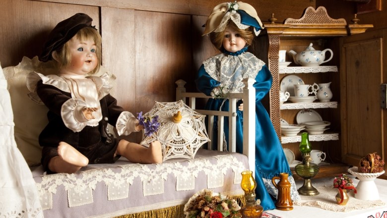 Zwei antike Puppen in einem nostalgischen Raum mit Geschirr und Dekorationen.