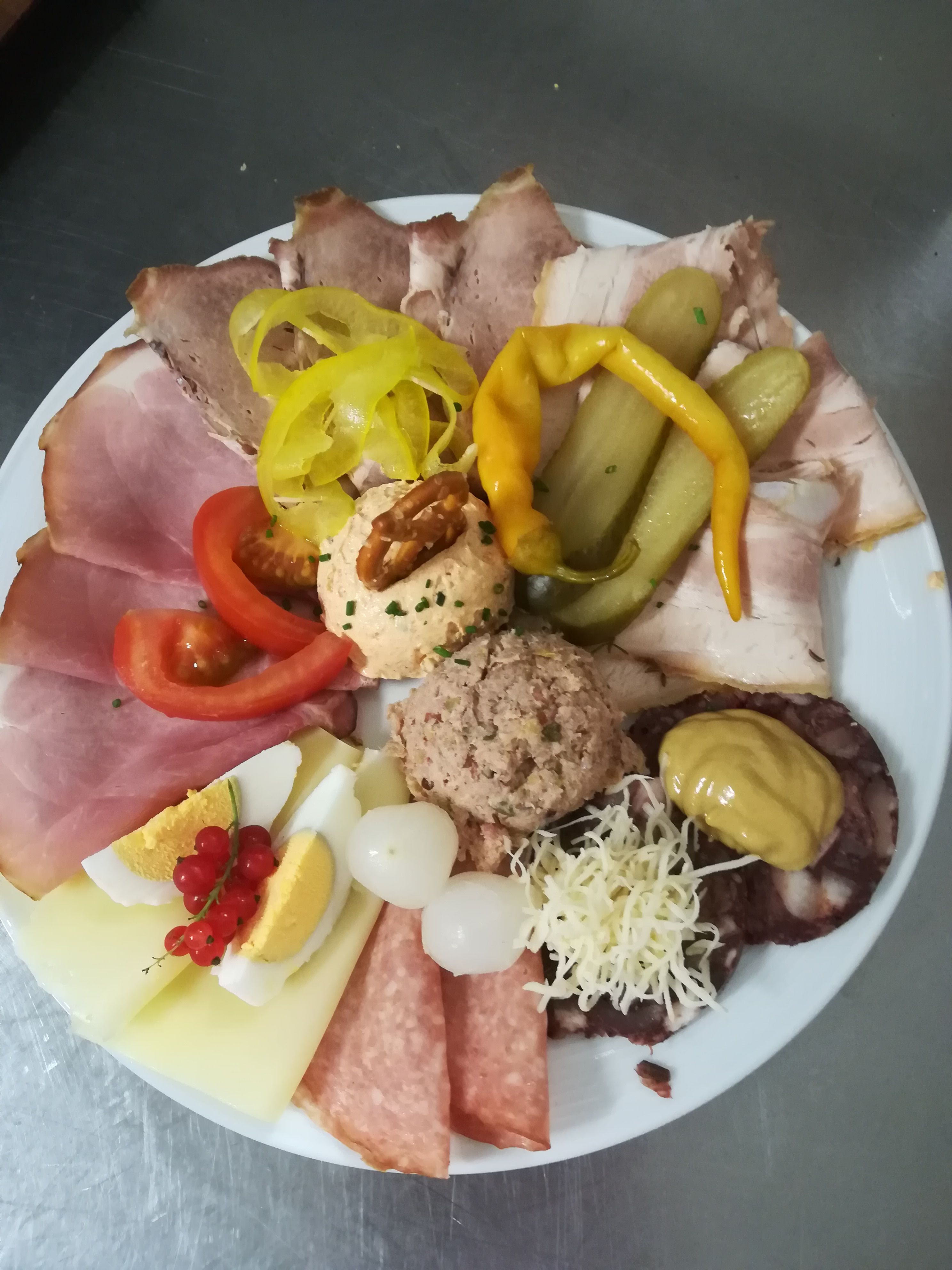 Ein Teller mit verschiedenen Wurst- und Käsesorten, Eiern, Zwiebeln, Paprika und Aufstrichen.