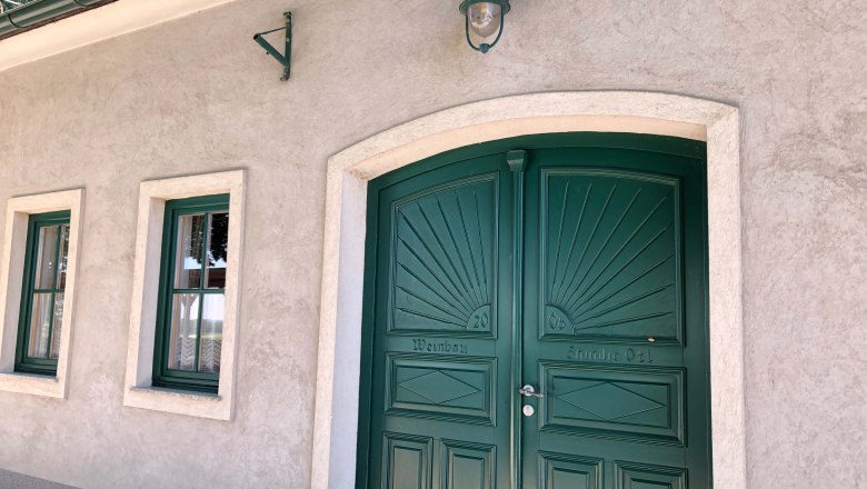 Green gate and windows of a wine tavern with a beige façade.