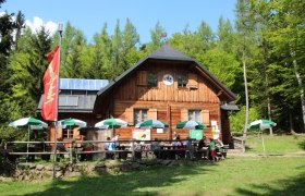 Holzhütte im Wald mit Sonnenschirmen und Menschen auf der Terrasse.