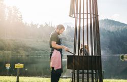 Ein Mann bereitet mit Hingabe ein köstliches Grillgericht am Ufer eines ruhigen Sees vor. Die sanften Hügel und die strahlende Sonne schaffen eine einladende Atmosphäre, die zum Verweilen einlädt. Hier, umgeben von der Schönheit der Natur, wird der Sommer in den Bergen zum unvergesslichen Erlebnis.