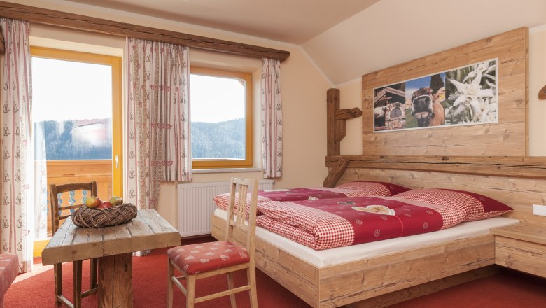 Gemütliches Zimmer im Alpenstil mit Holzmöbeln, rotem Teppich und Bergblick.