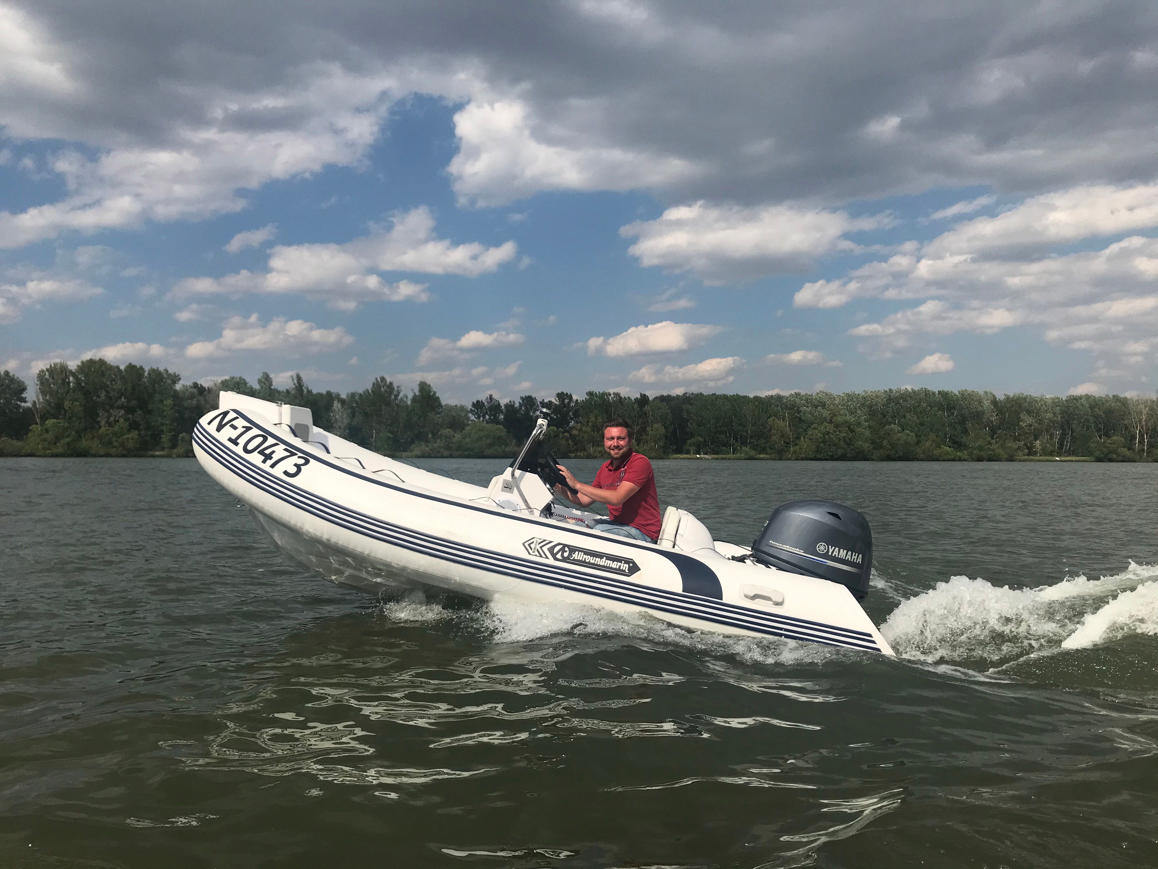 Ein Mann fährt ein Schlauchboot mit Yamaha-Motor auf einem See, umgeben von Bäumen und unter einem bewölkten Himmel.