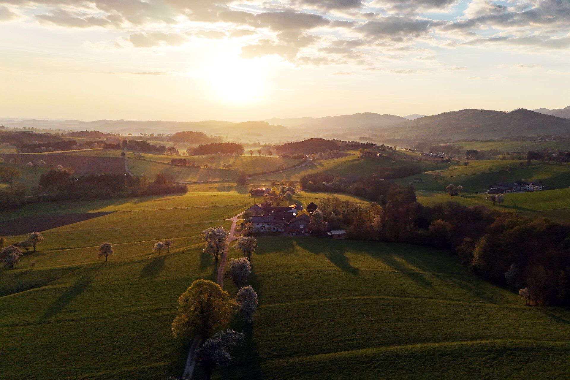 Luftaufnahme einer hügeligen Landschaft bei Sonnenuntergang.