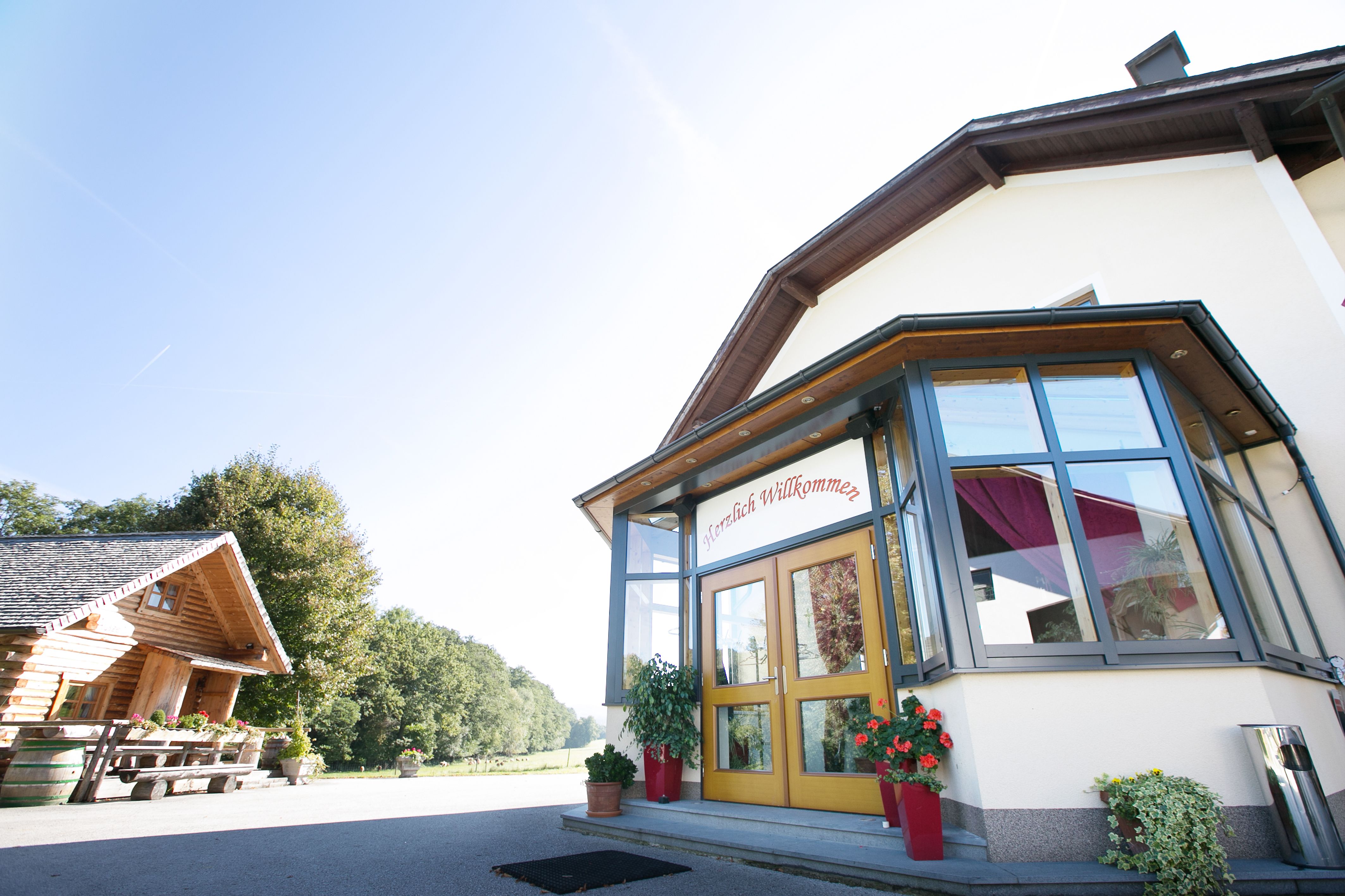 Eingang eines Gebäudes mit Glasveranda und "Herzlich Willkommen"-Schild.