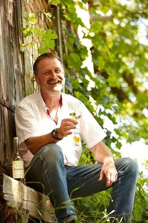 Mann sitzt draußen mit einem Glas Wein in der Hand, umgeben von grünen Pflanzen.