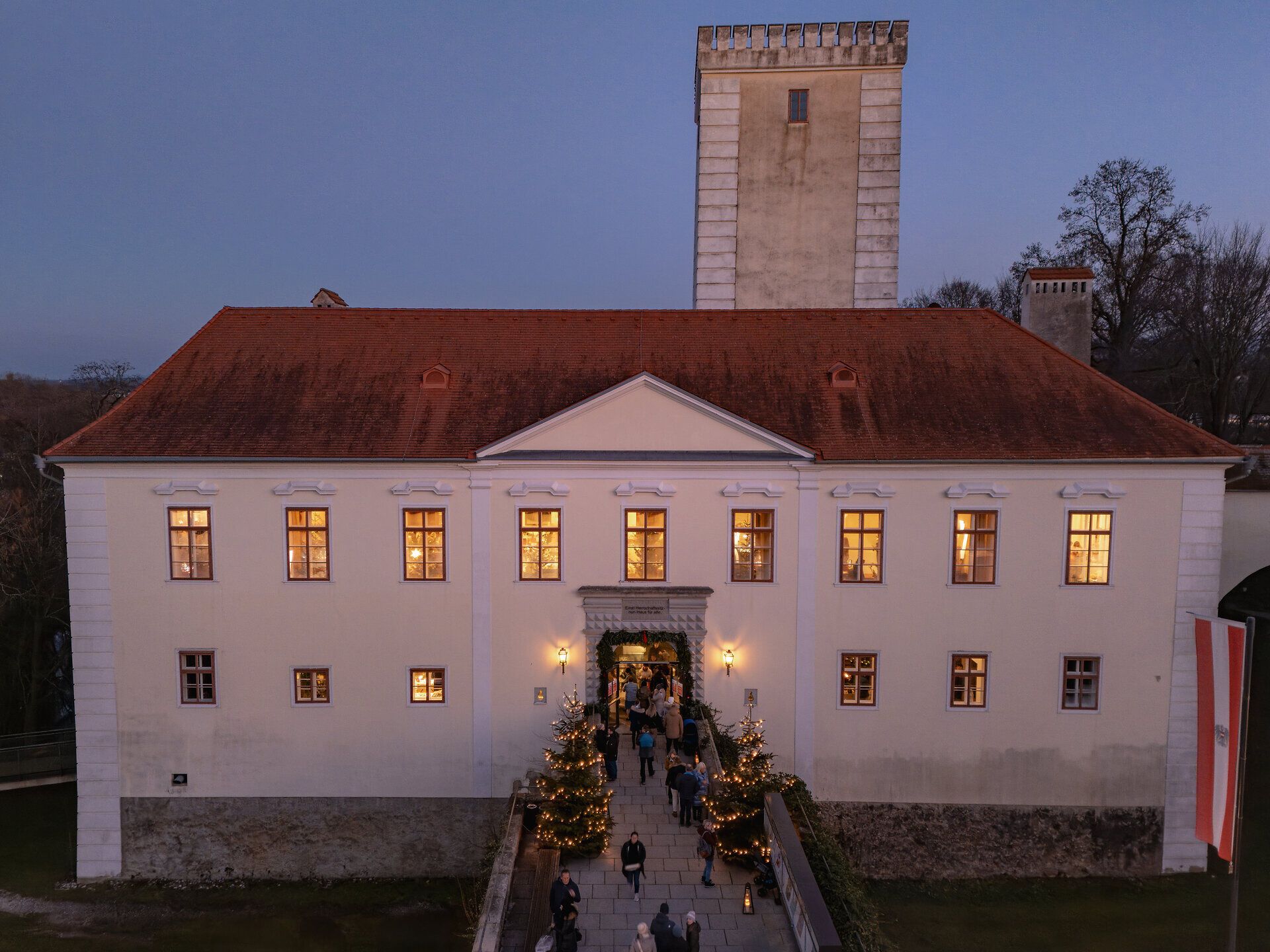 Beleuchtetes Schloss mit Besuchenden des Adventmarkts im Innenhof. 