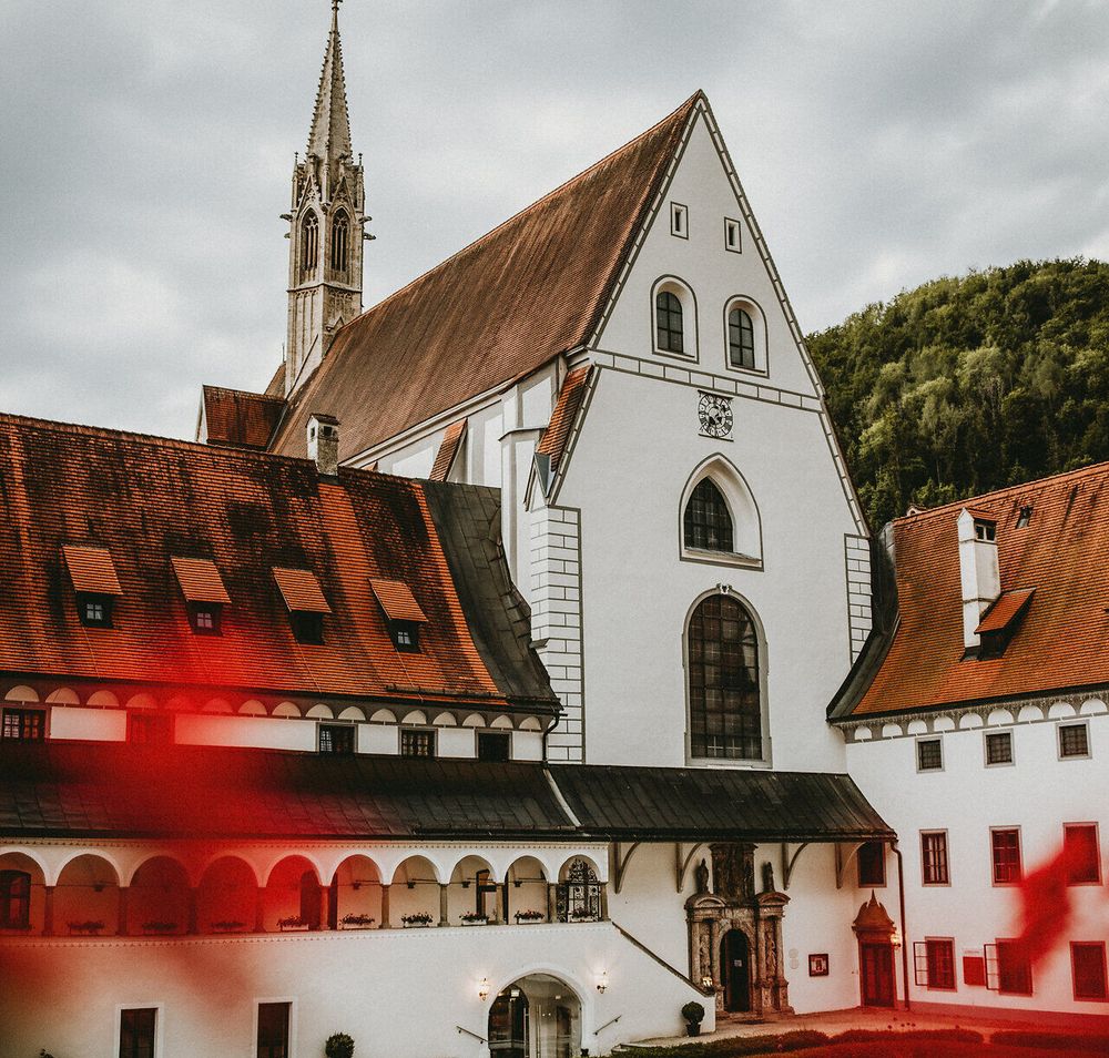 Die majestätische Kartause Gaming erhebt sich stolz zwischen sanften Hügeln, umgeben von üppigem Grün und blühenden Pflanzen. Die beeindruckende Architektur des Klosters strahlt Ruhe und Gelassenheit aus, während die Wolken am Himmel eine dramatische Kulisse schaffen. Ein Ort, der zum Verweilen und Entdecken einlädt.