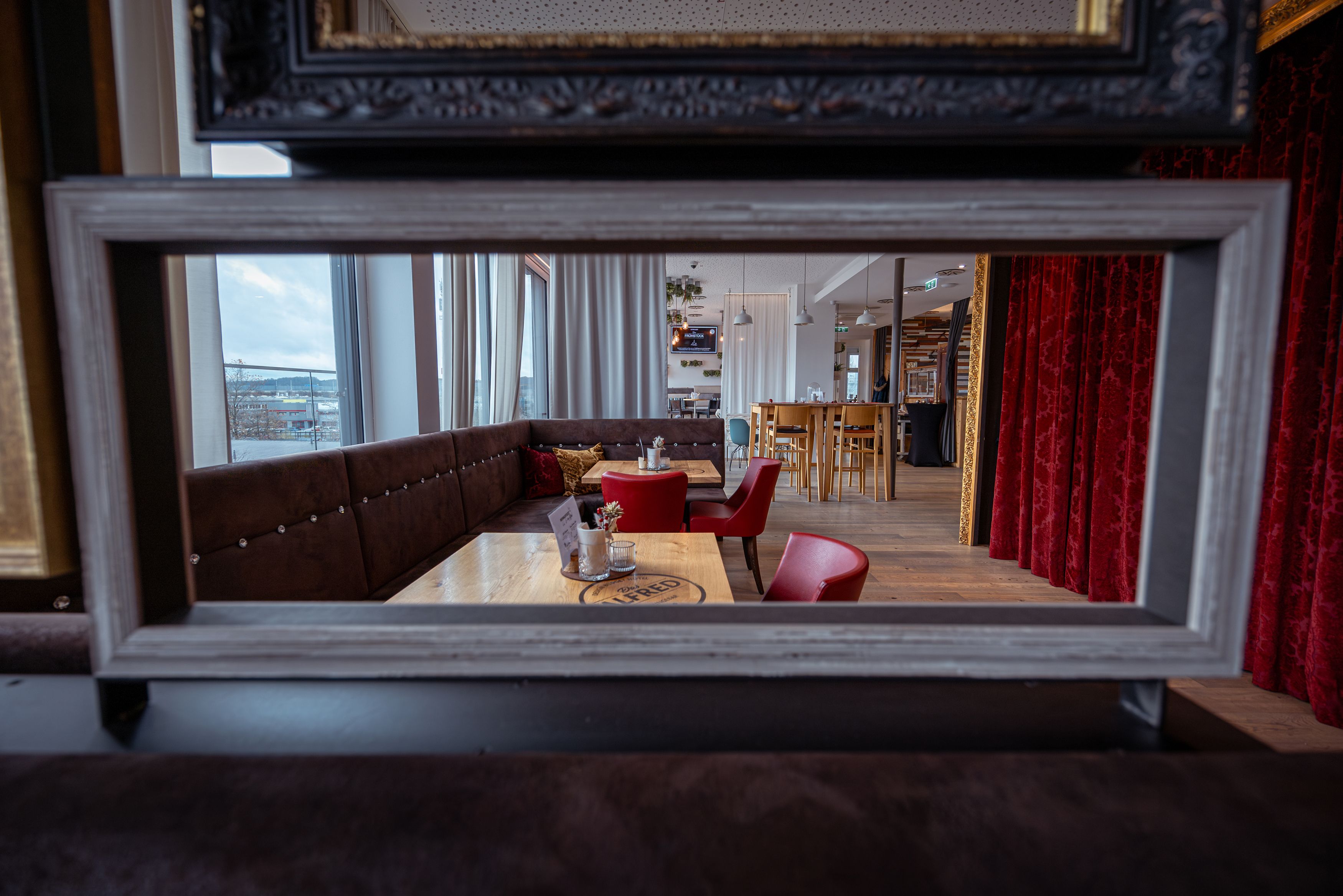 Innenansicht eines stilvollen Cafés mit roten Stühlen und Holztischen, gesehen durch einen Bilderrahmen.