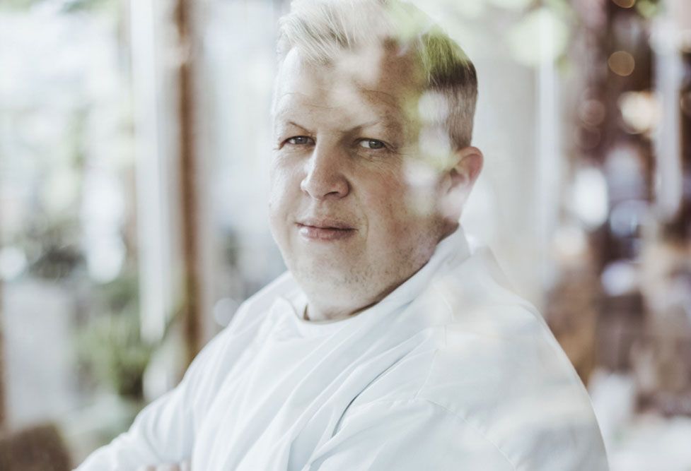 Porträt eines Mannes in weißem Hemd, durch ein Fenster fotografiert.