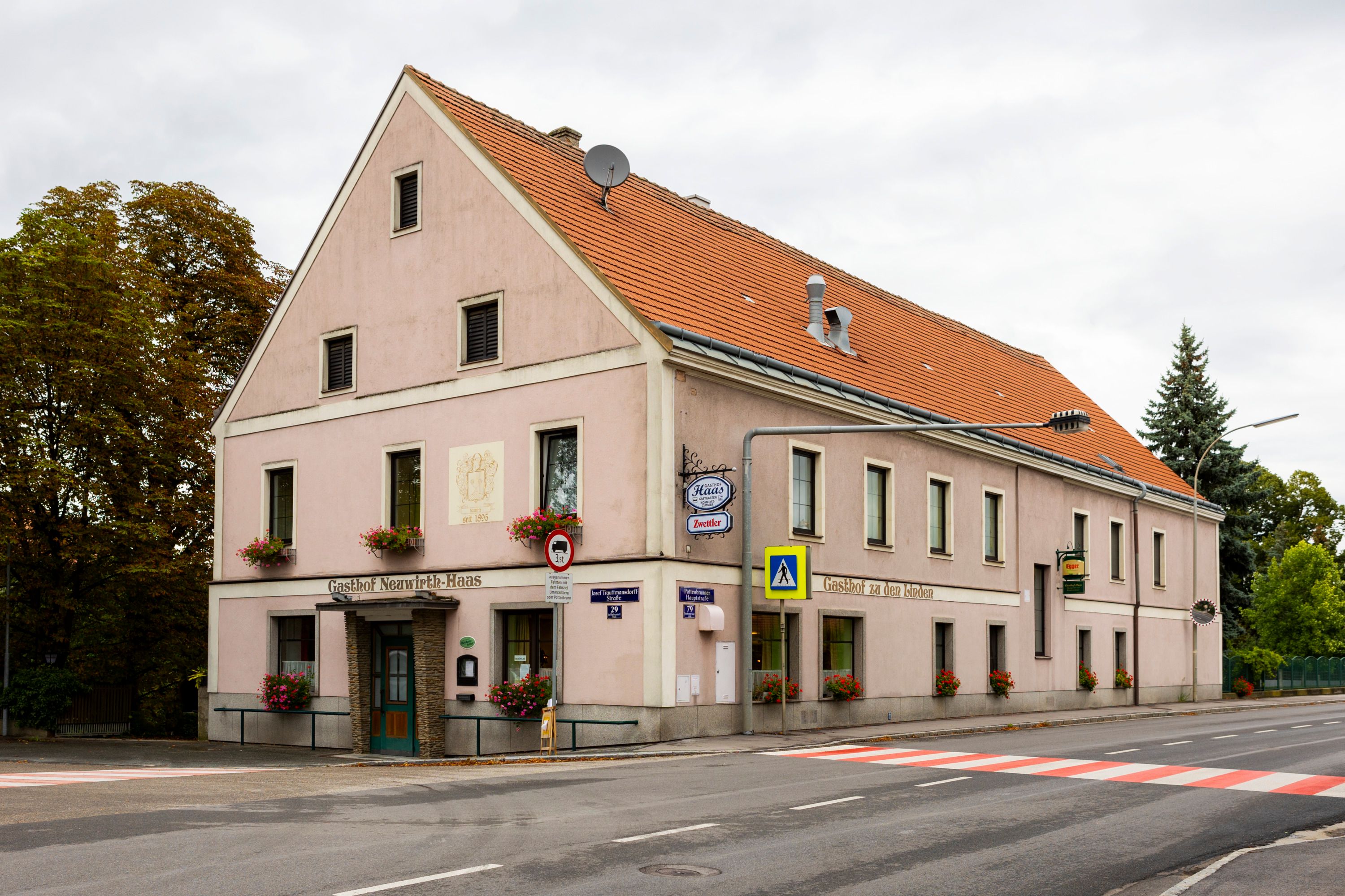 Ein traditionelles Wirtshaus mit rosa Fassade und roten Dachziegeln an einer Straßenecke in Pottenbrunn.