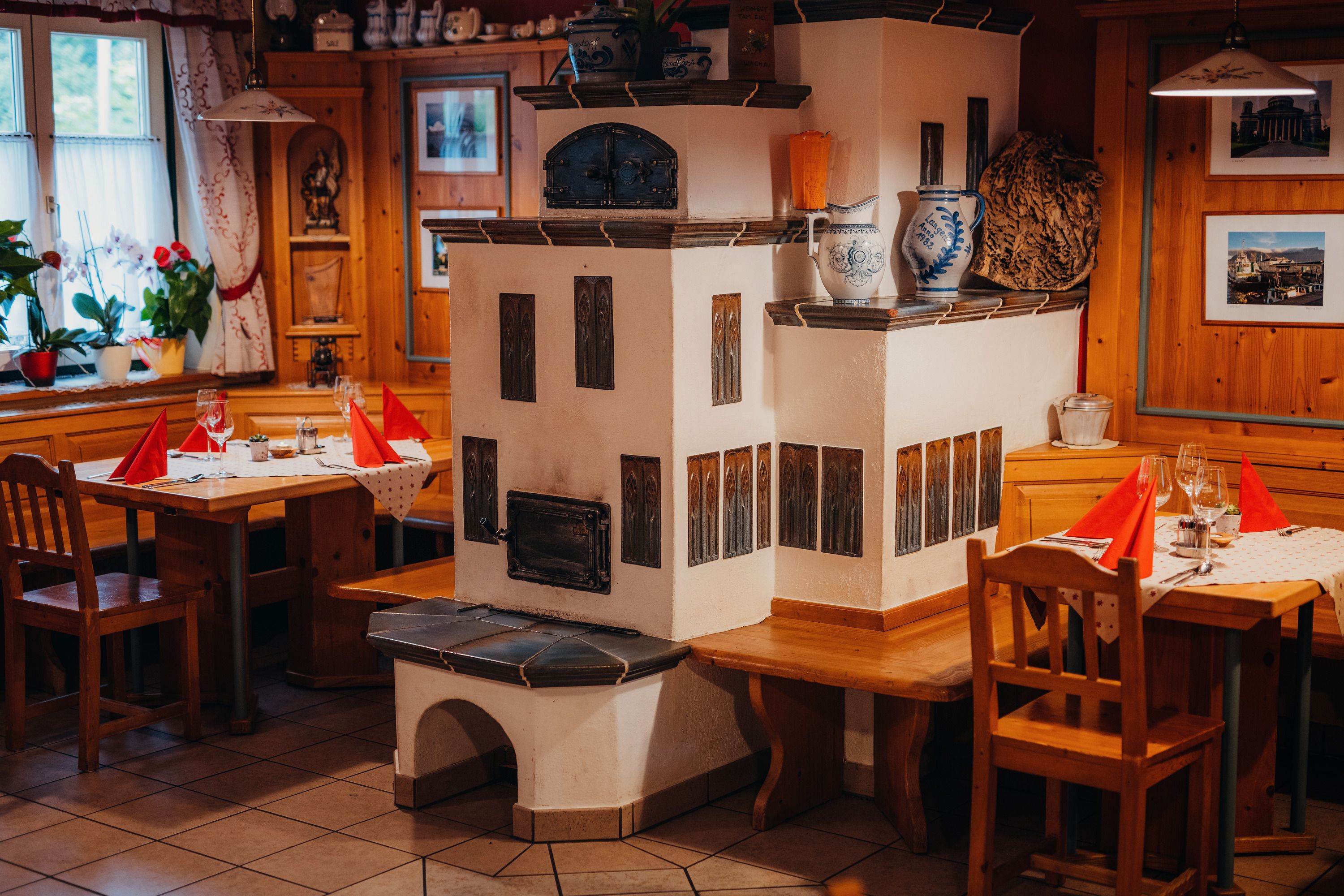 Gemütliche Stube mit Kachelofen, Holzmöbeln und gedeckten Tischen.