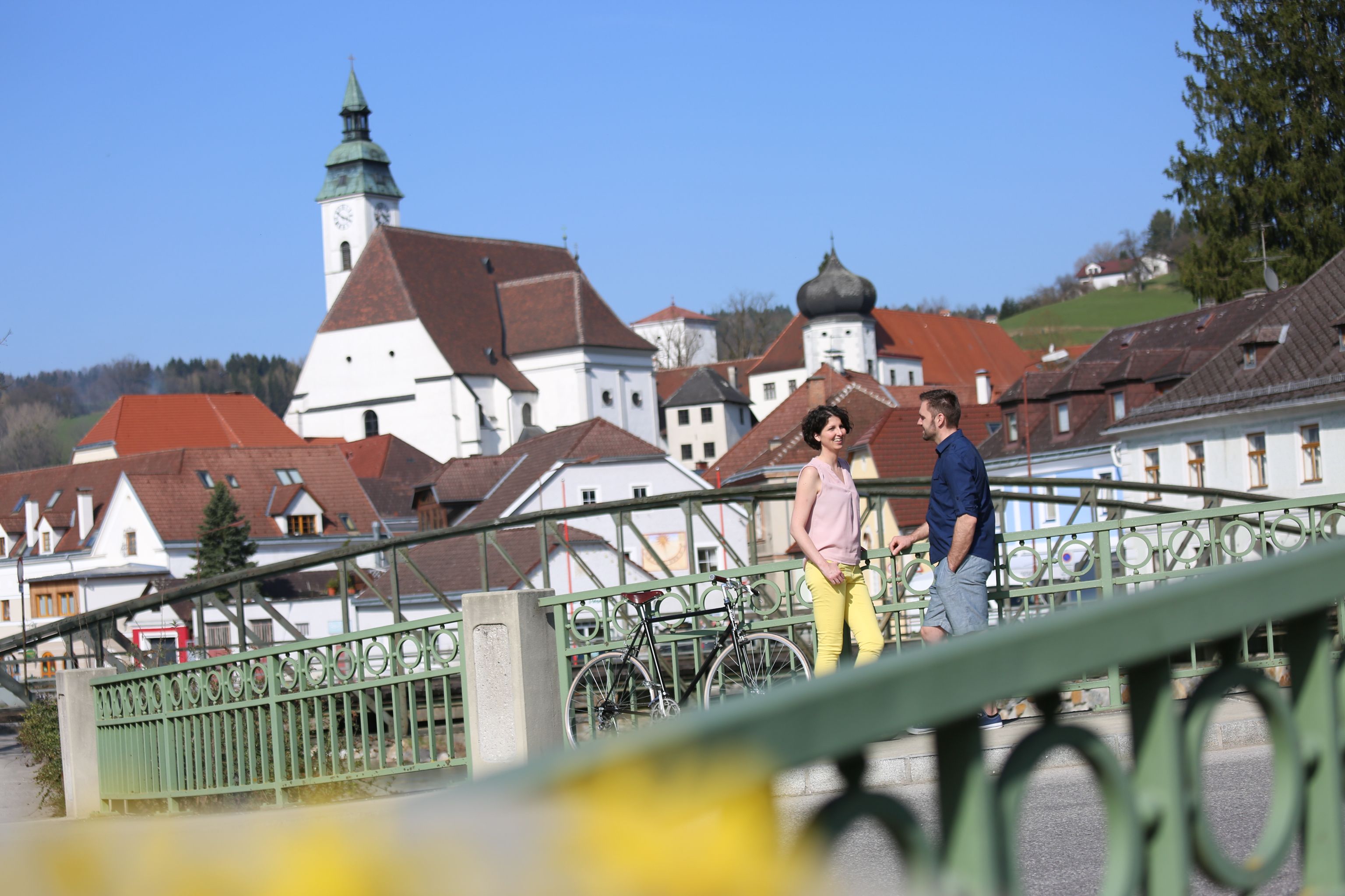 Ein Paar steht auf einer Brücke in Scheibbs mit einer Kirche im Hintergrund.