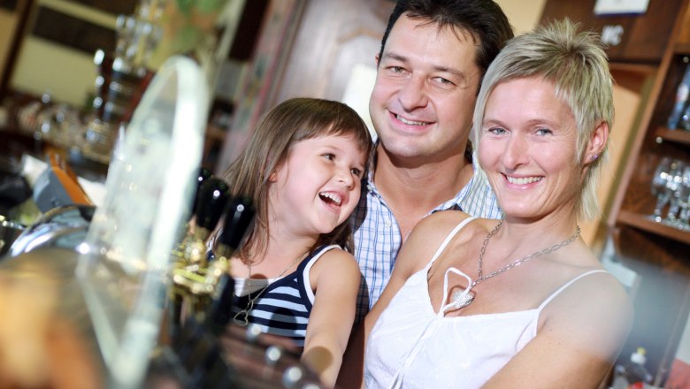 Eine lächelnde Familie steht in einem Restaurant oder Hotel an der Bar.