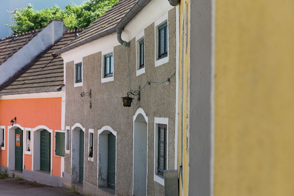 Bunte Häuser in einer Kellergasse mit grünen Türen und Fenstern.