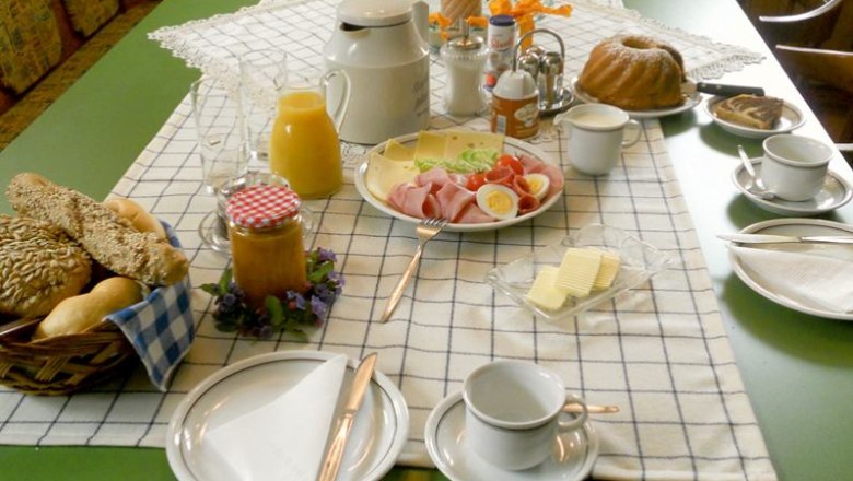 A laid breakfast table with bread rolls, cold cuts, cheese, juice, coffee and cake.