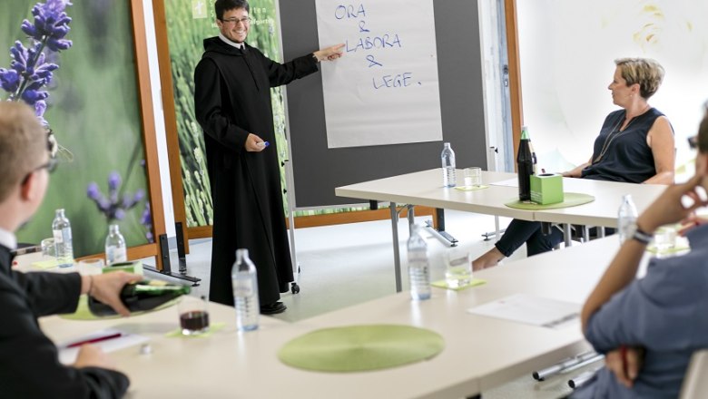 Ein Seminar im Stift Seitenstetten mit einem Vortragenden in M&ouml;nchskleidung, der auf ein Flipchart zeigt. Teilnehmer sitzen an Tischen.