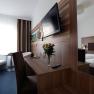 Modern furnished hotel room with double bed, desk, flat screen TV and bouquet of flowers.
