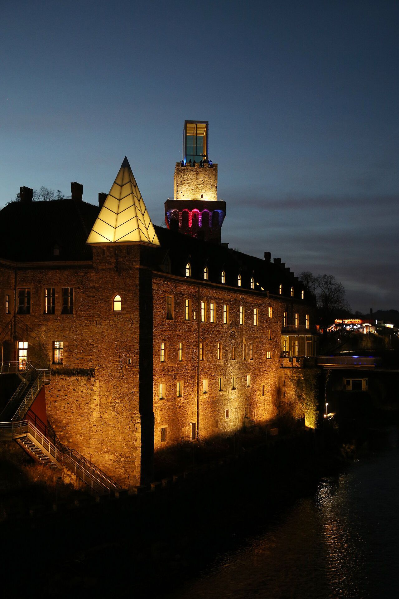 In der sanften Dämmerung erstrahlt das Schloss Rothschild in warmen Lichttönen, während der Fluss leise plätschert. Die harmonische Verbindung von historischer Architektur und modernem Design schafft eine magische Atmosphäre, die zum Verweilen einlädt.