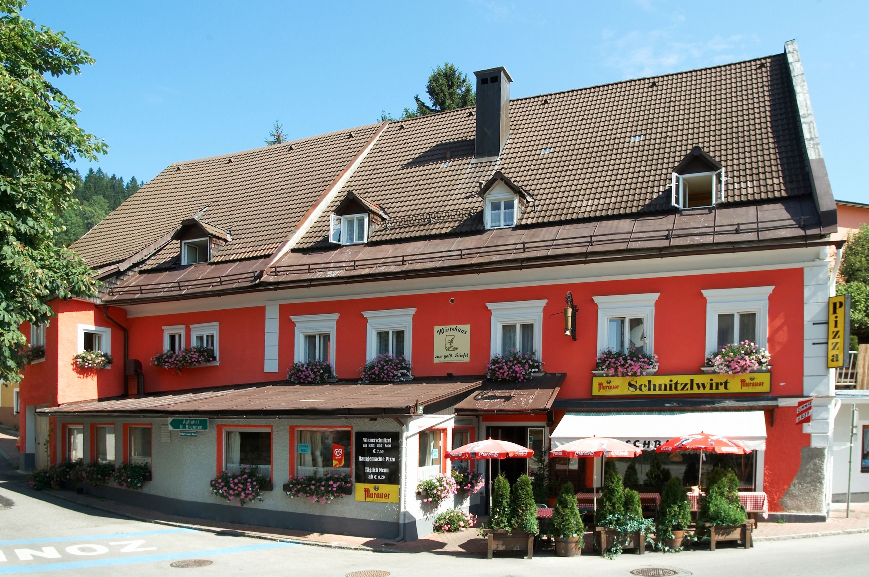 Ein traditionelles Gasthaus mit roter Fassade und Blumenkästen, beschriftet als 'Schnitzlwirt'.