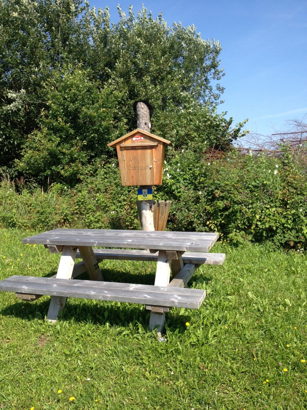 Picknicktisch neben einem Bildstock auf einer Wiese mit Bäumen im Hintergrund.
