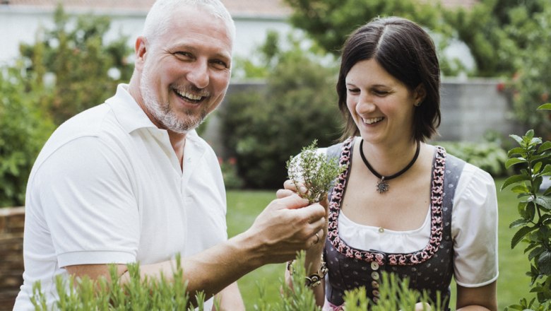 A man and a woman stand smiling in a garden looking at herbs.