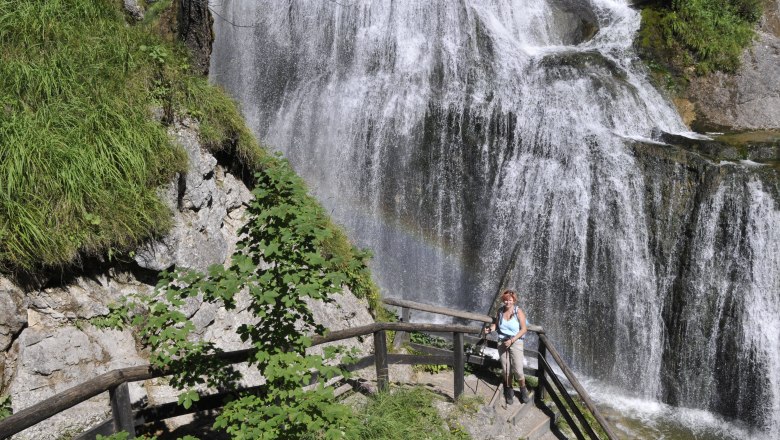 A woman stands on a staircase in front of a waterfall in the Palfau waterhole gorge.