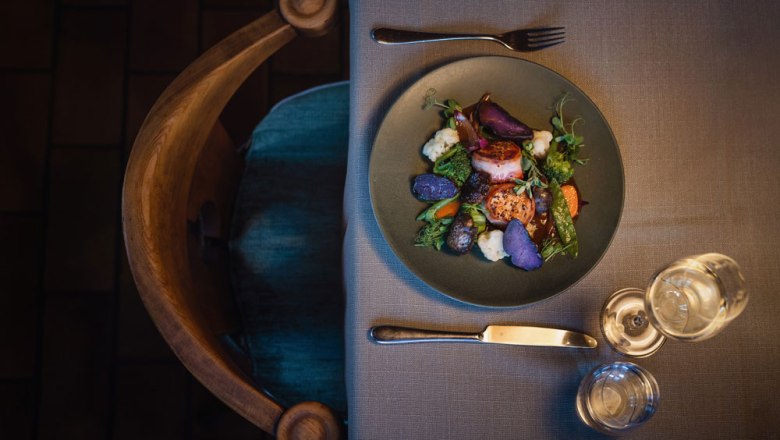 A plate of pork medallions, purple potatoes and vegetables on a laid table.