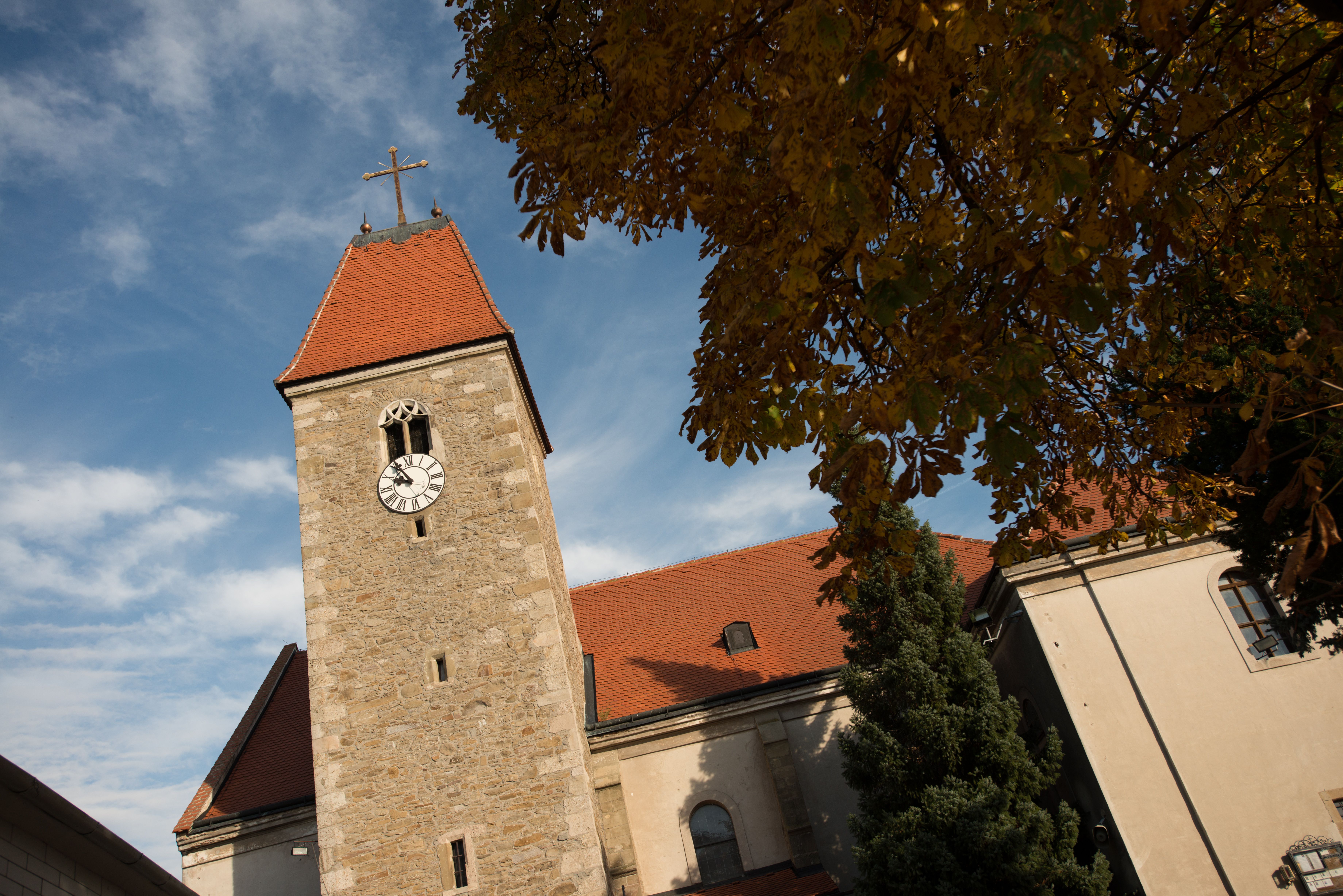 Kirchturm der Kirche Weißenkirchen mit Uhr und rotem Dach, umgeben von Herbstlaub und blauem Himmel.
