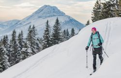 Eine Frau genießt die frische Winterluft auf ihrer Skitour und lässt sich von der atemberaubenden Aussicht auf die schneebedeckten Berge verzaubern. Die unberührte Schneelandschaft und die majestätischen Tannen schaffen eine friedliche Atmosphäre, die zum Verweilen einlädt.
