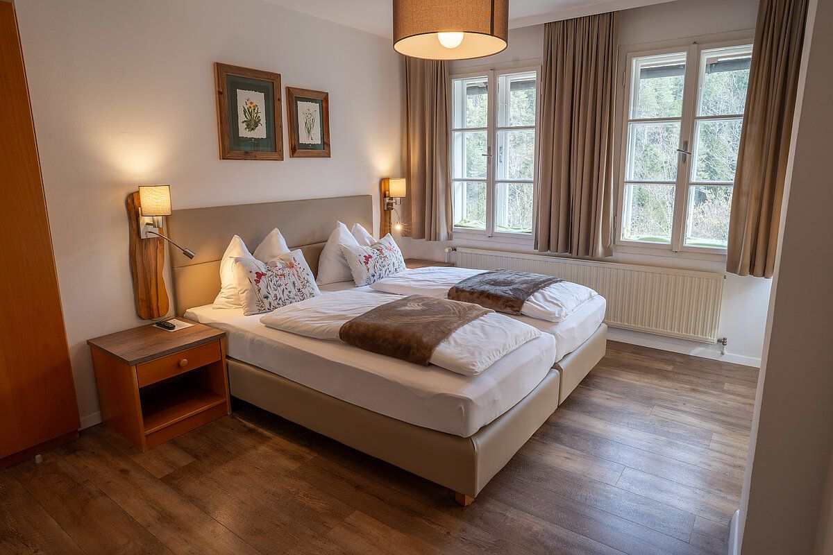 Ein gemütliches Schlafzimmer mit zwei Einzelbetten, Holzboden und großen Fenstern mit Blick auf die Natur.