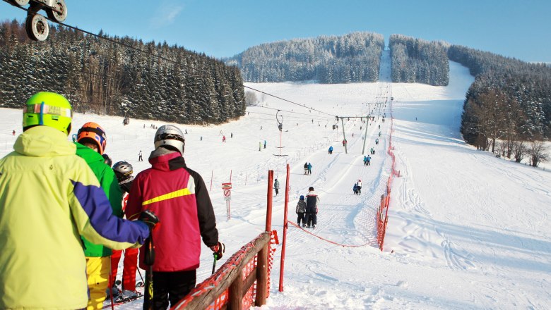 Skiers stand in a queue at the ski lift on a snowy slope.