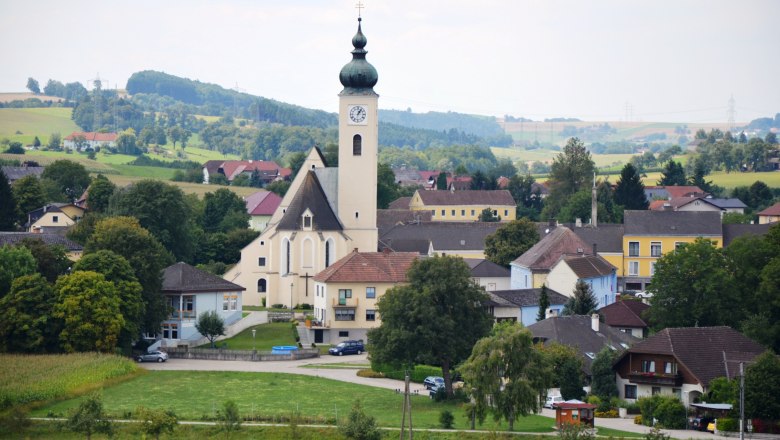 Blick auf die Marktgemeinde Ruprechtshofen mit Kirche und umliegenden Häusern in einer ländlichen Landschaft.