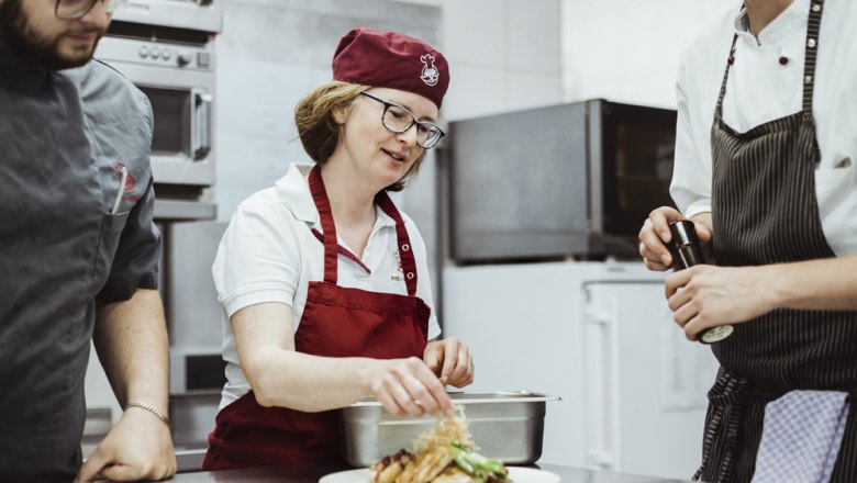 Three chefs in a restaurant kitchen prepare a dish.