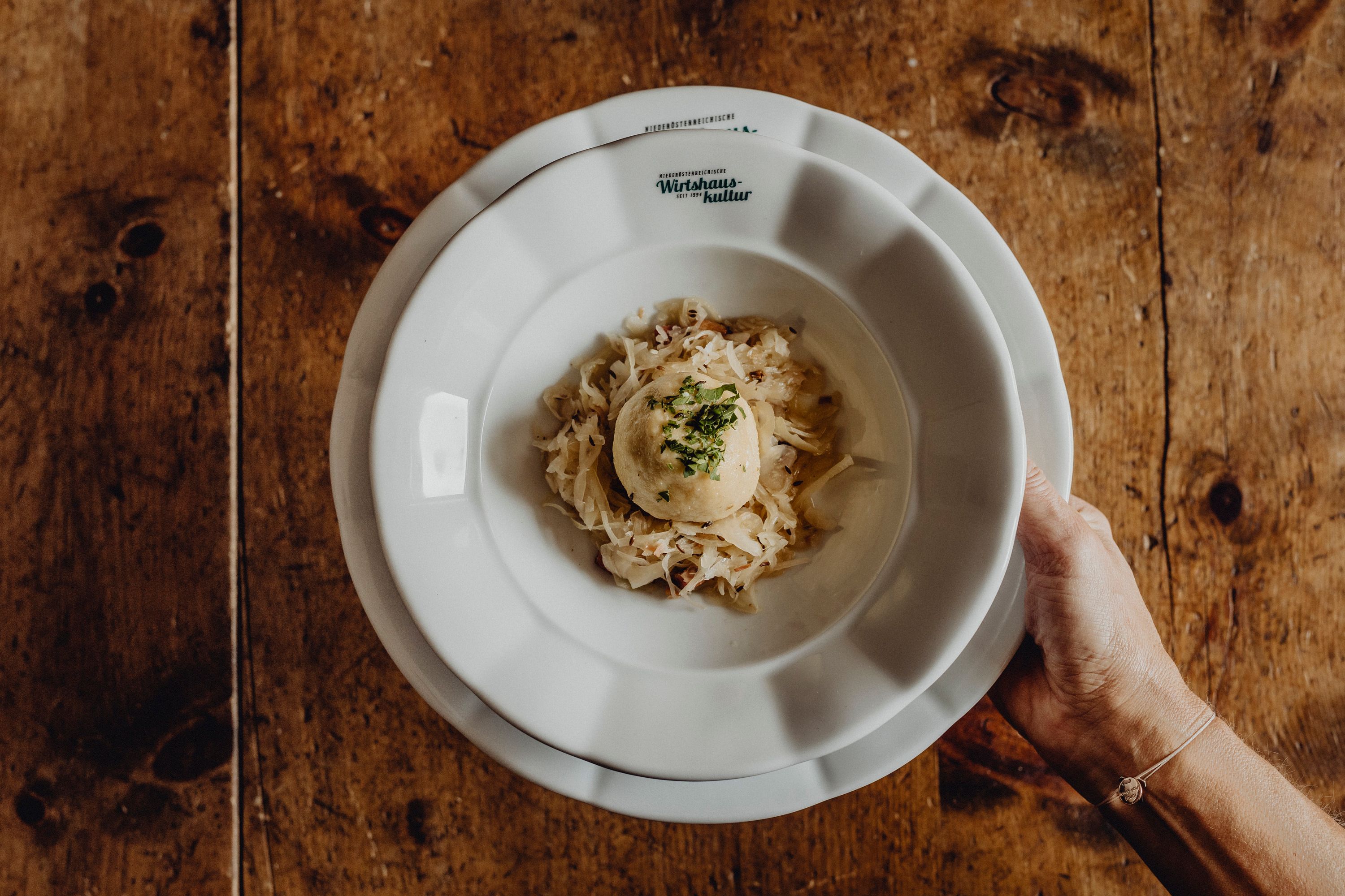 Ein Teller mit einem Grammelknödel auf Sauerkraut, gehalten von einer Hand.
