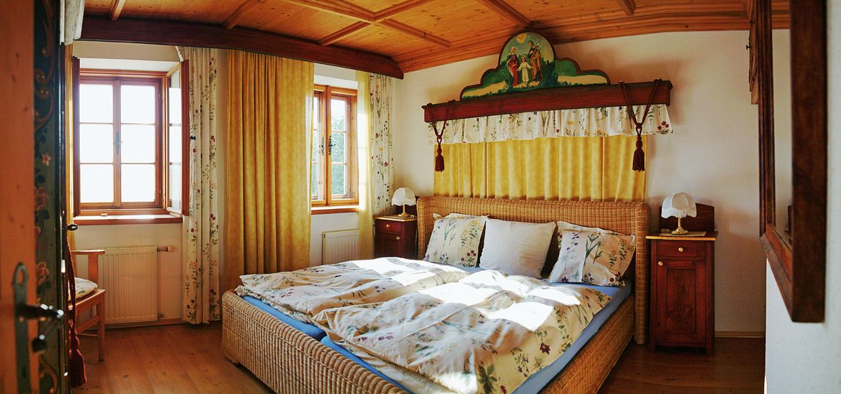 Gemütliches Schlafzimmer mit Holzmöbeln und Doppelbett, dekoriert mit floralen Mustern und gelben Vorhängen.