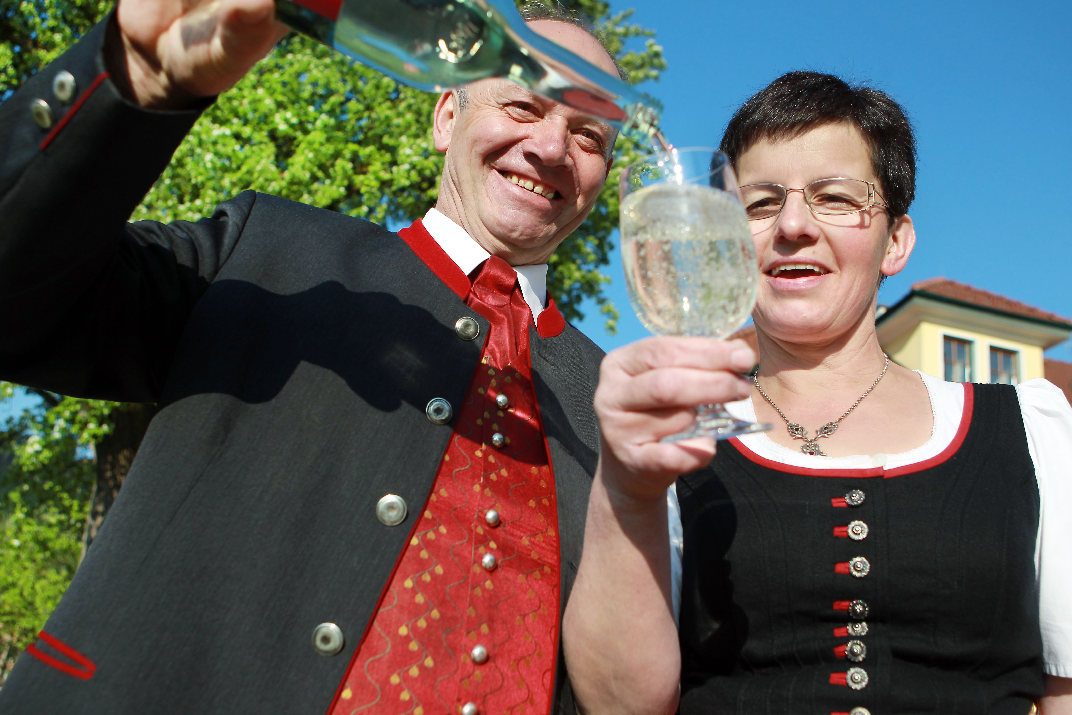 Zwei Personen in traditioneller Kleidung stoßen mit einem Glas an, während eine Flasche eingeschenkt wird.